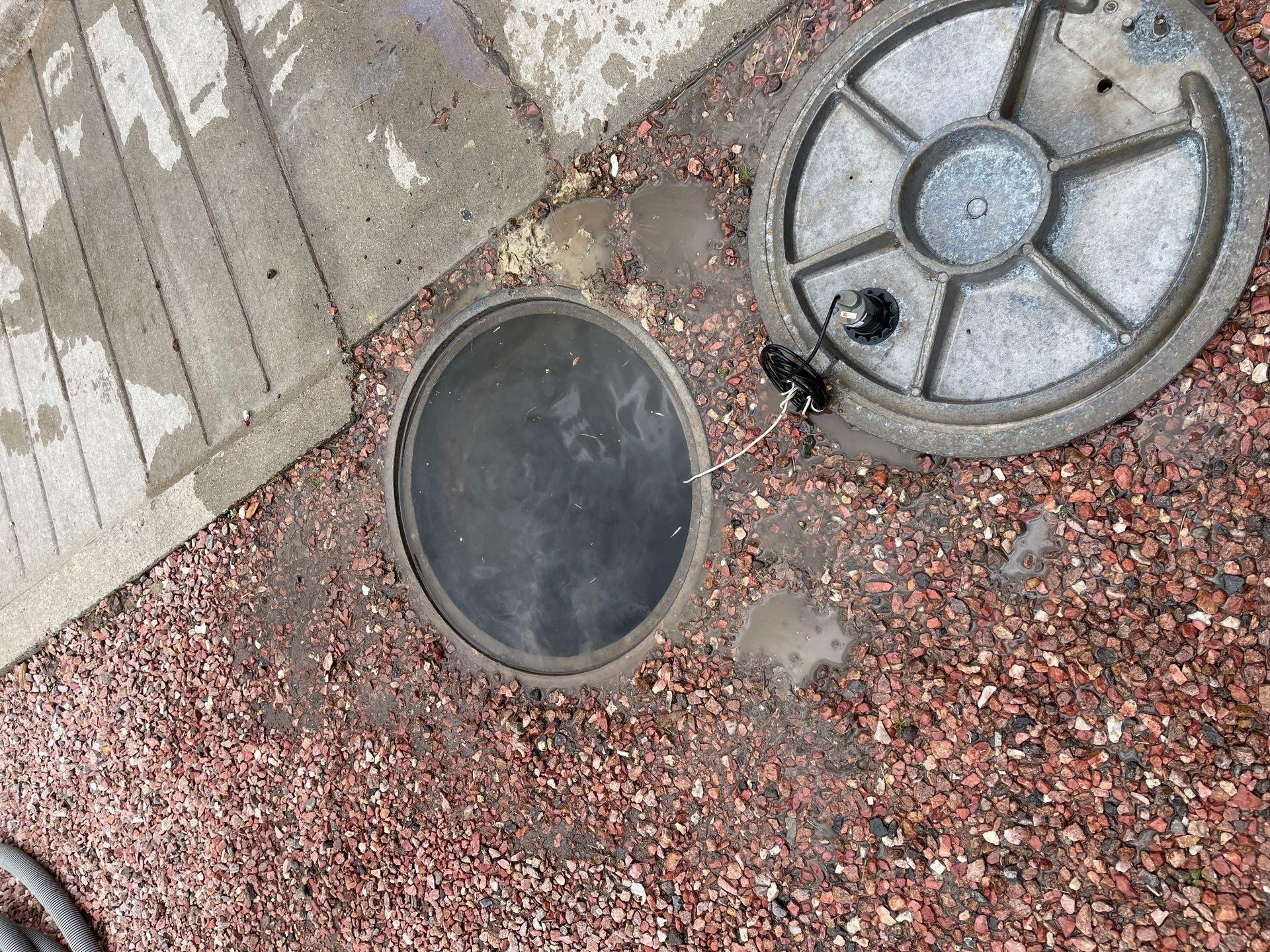 Two round manhole covers set in red gravel beside a concrete sidewalk edge