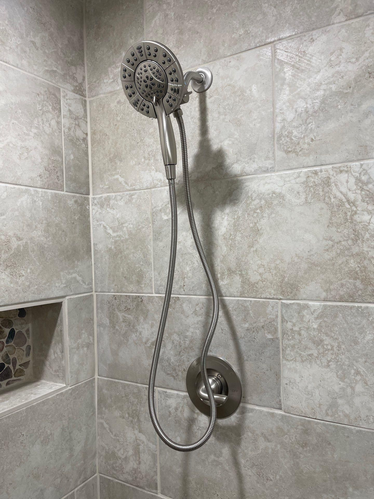 Chrome showerhead and handheld shower sprayer in a tiled shower stall.