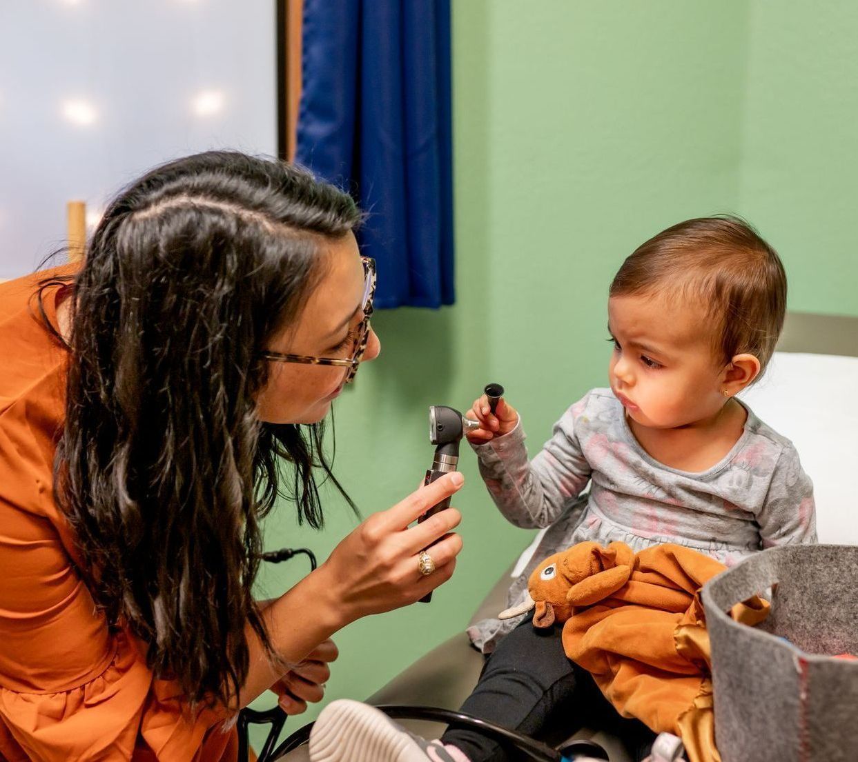 A woman is examining a baby 's ear with a stethoscope.