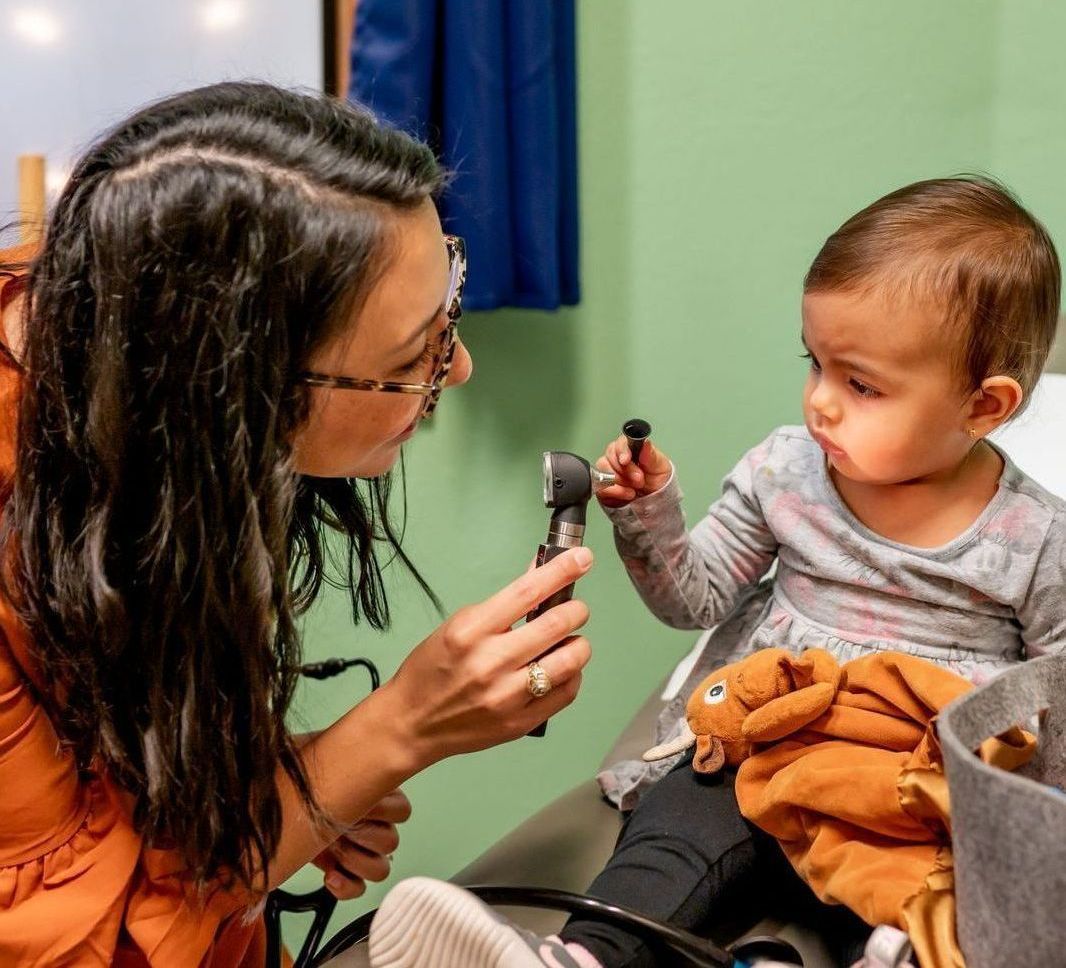 A woman is examining a baby 's ear with a stethoscope.