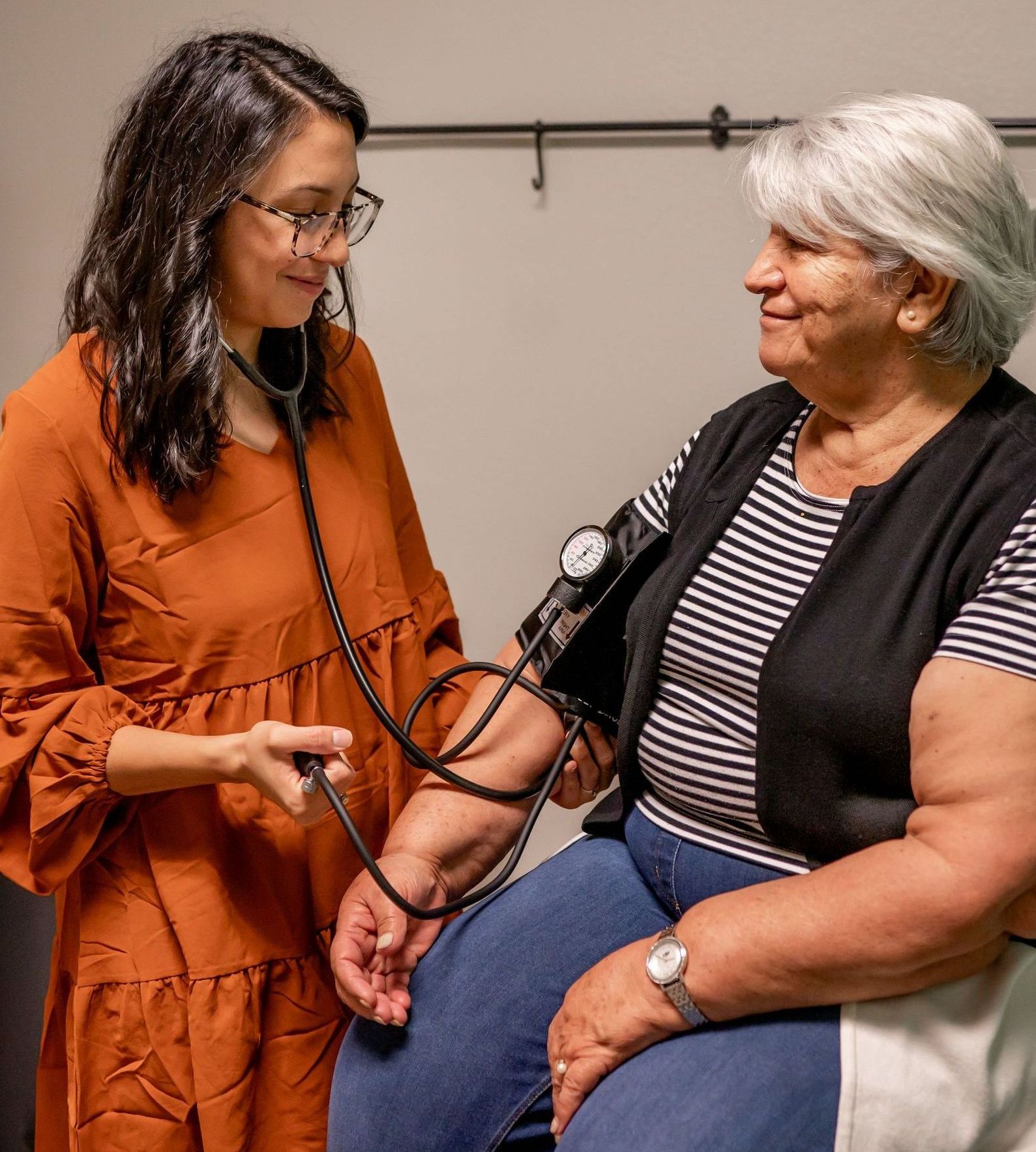 Doctor checking patient's blood pressure with stethoscope. Clinic setting, both smiling.