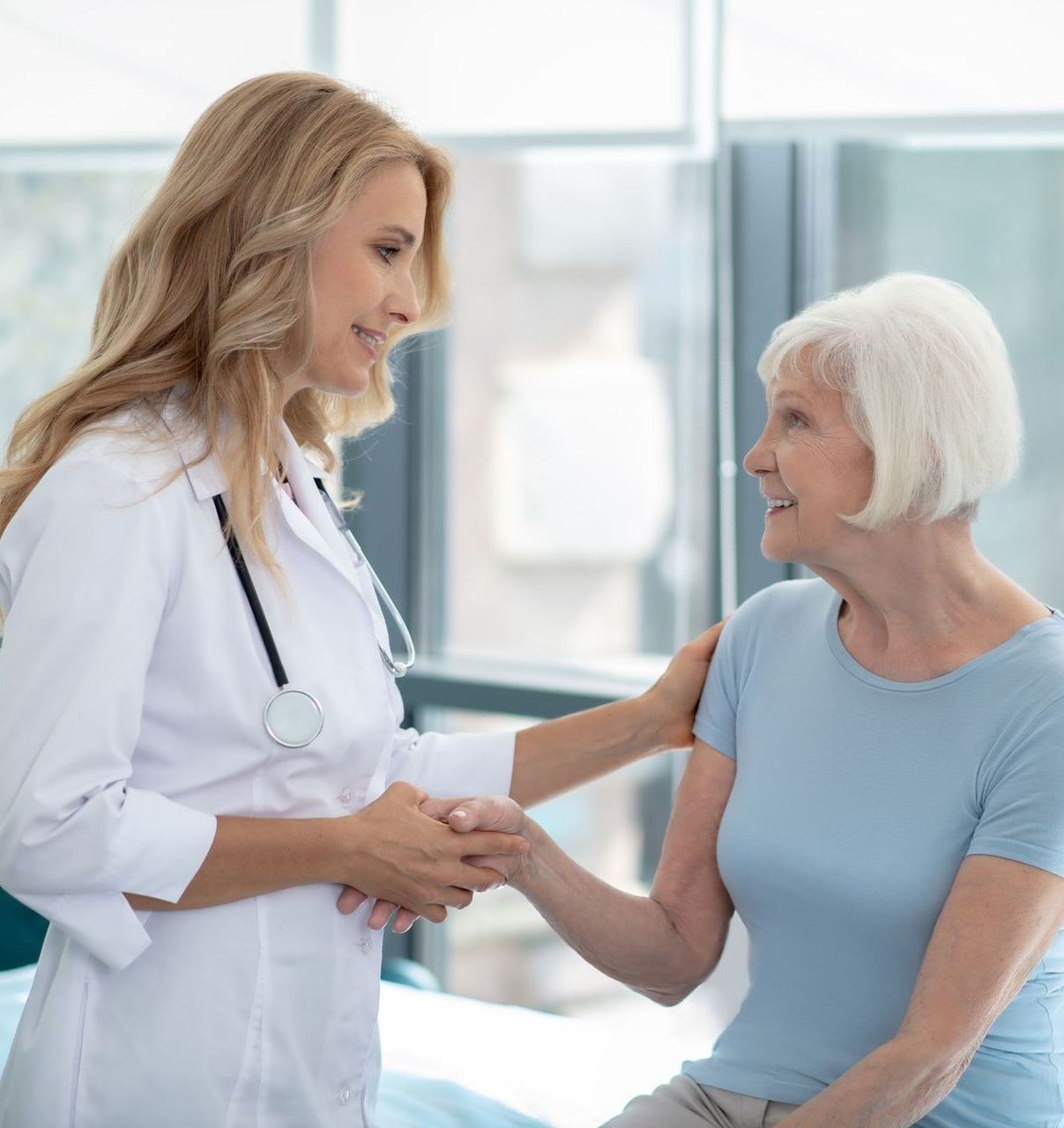 A doctor is shaking hands with an elderly woman in a hospital bed.