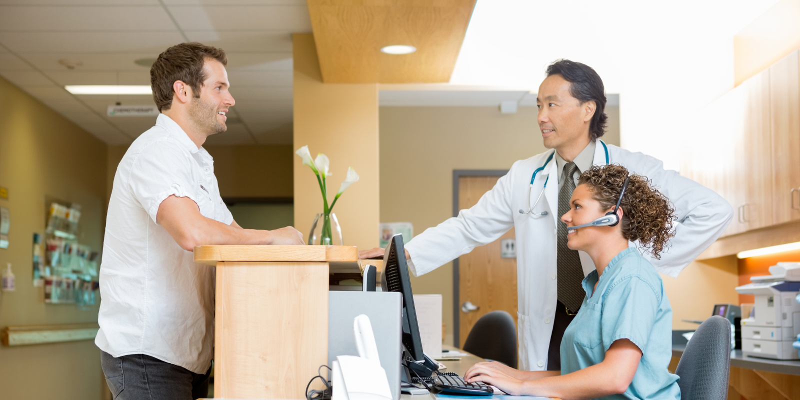 patient in an DPC office greeting receptionist around a desk with a computer.