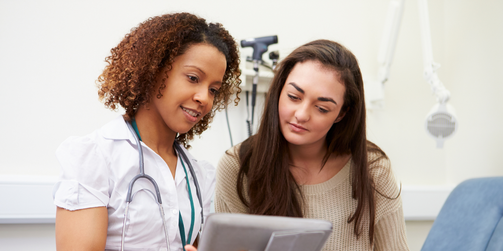 Two women reviewing a document in a clinic, one wearing a white coat and stethoscope.