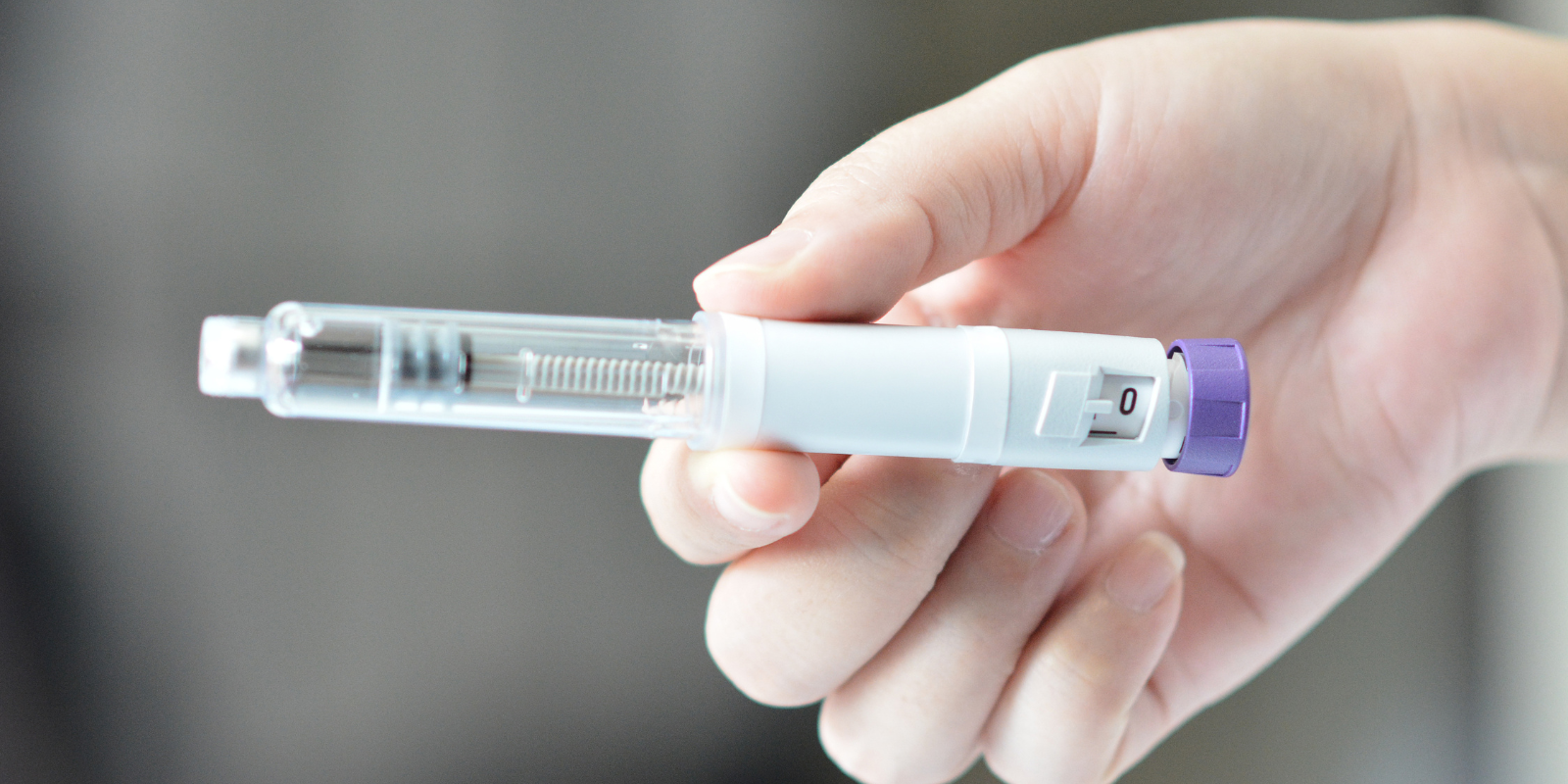 Hand holding a small clear syringe with a purple cap against a white background