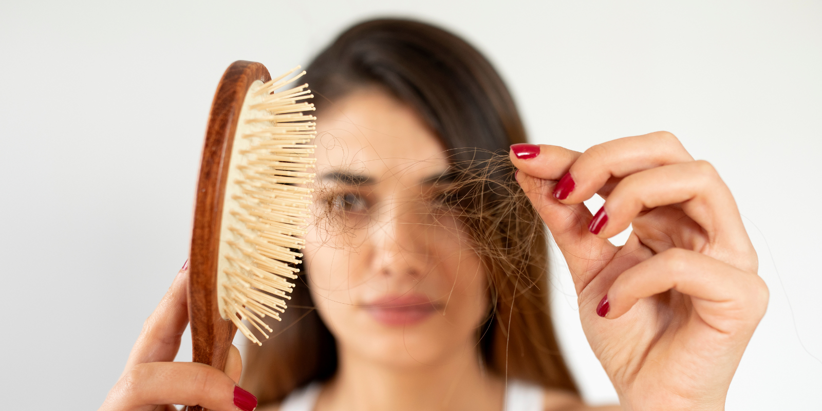 Woman holding a hairbrush and pulling out loose hair, showing hair loss close-up
