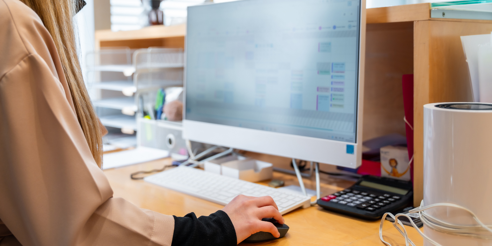 Person working at a desk with a computer monitor and keyboard in a bright office