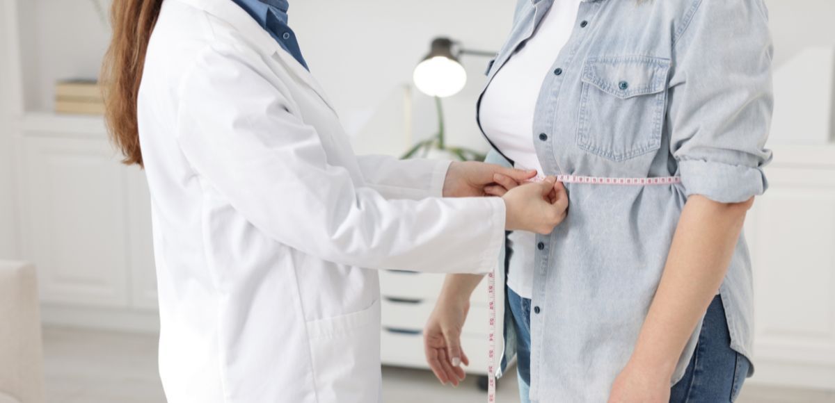 Doctor measuring a patient’s waist with a tape in a bright clinic room