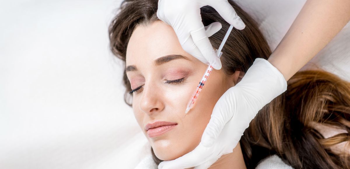 Cosmetician applying brow treatment to a woman with closed eyes using gloved hands