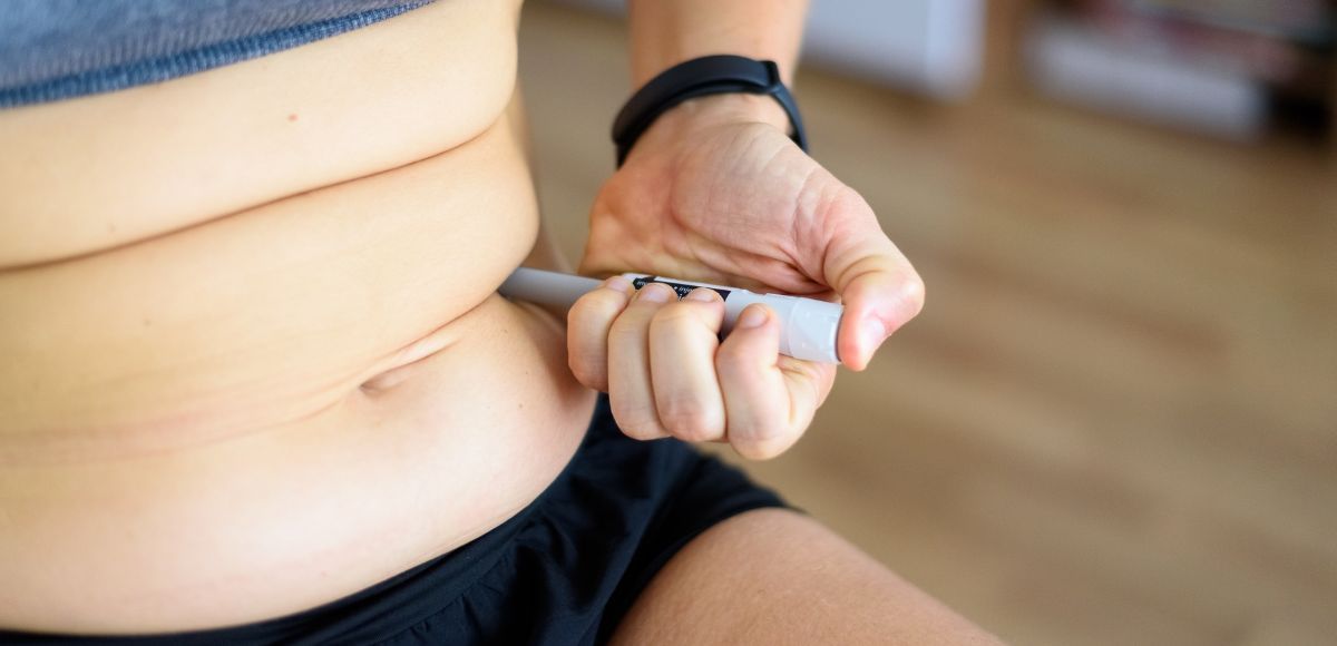 Person pinching abdominal fat with a hand in a black wristband and shorts