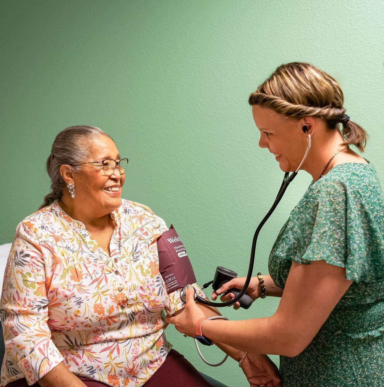 An older woman smiling as a healthcare professional checks her blood pressure
