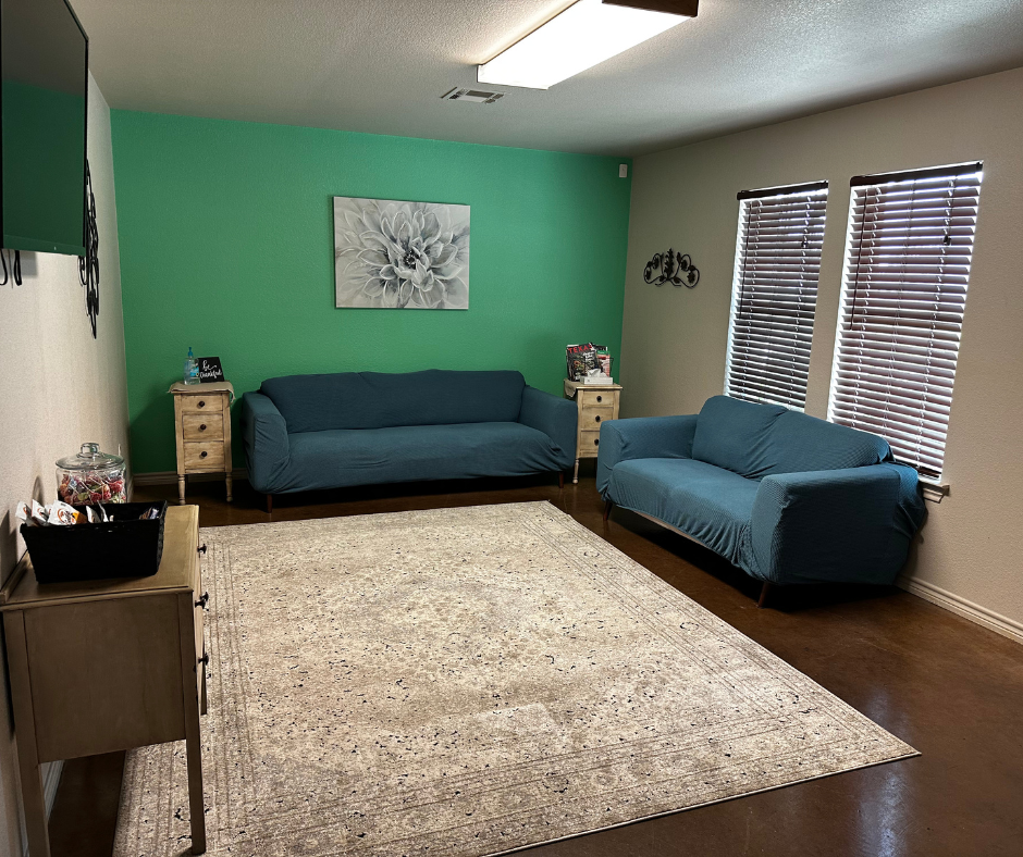 Living room with teal sofas, green accent wall, neutral rug, and two windows with blinds.