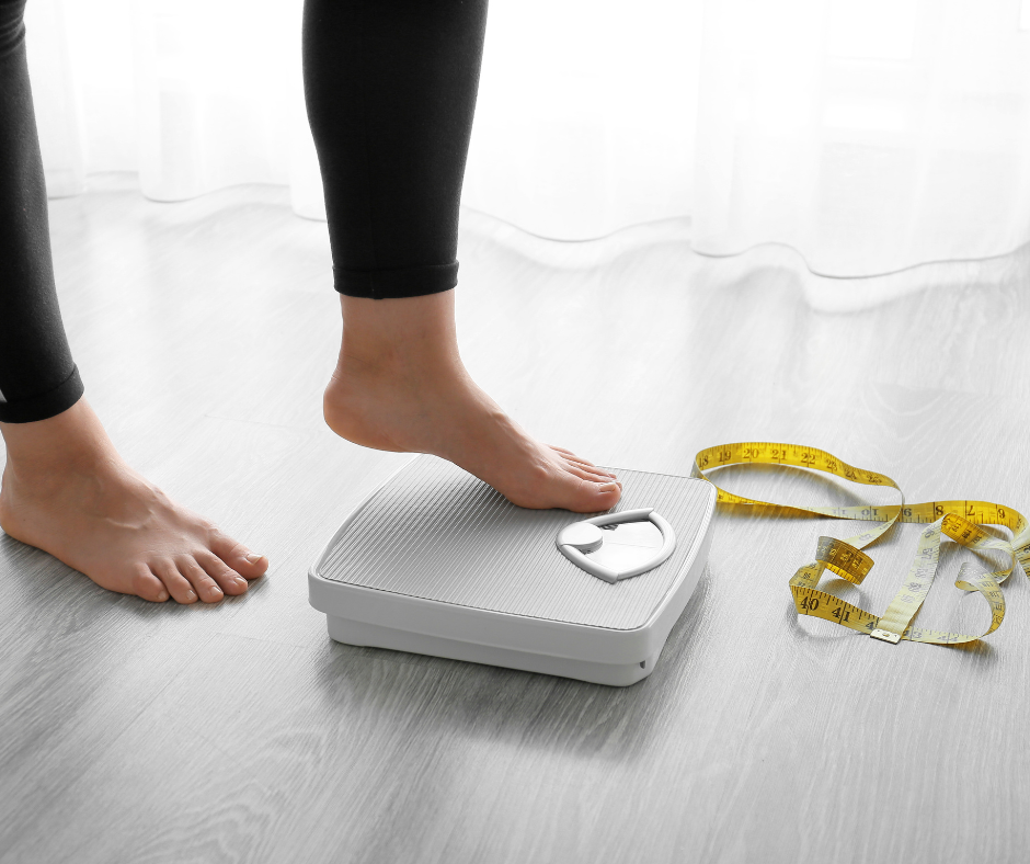 woman weighing herself on a scale, with a measuring tape on the floor beside it