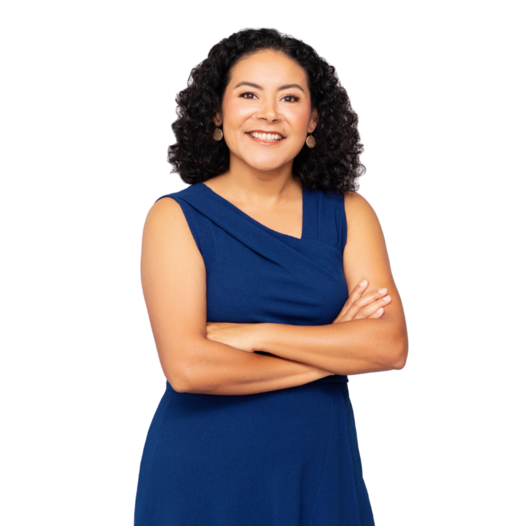 Woman with curly dark hair, wearing a blue sleeveless dress, arms crossed, smiling.