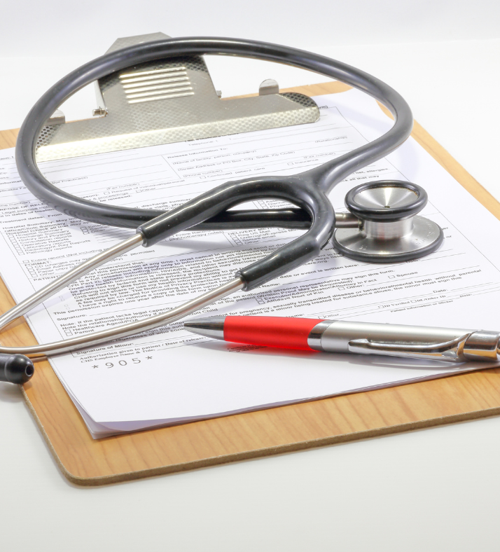 Stethoscope, clipboard with medical forms, and a pen on a light brown wooden surface.