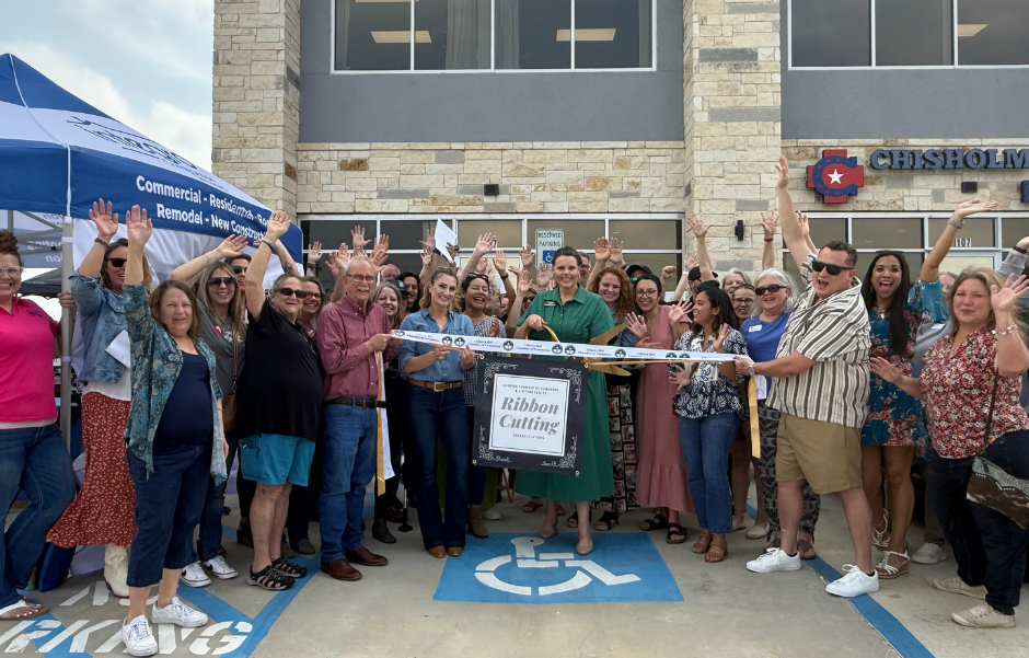 Group of people celebrating a ribbon-cutting ceremony in front of a building with a blue awning.