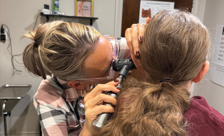 A healthcare provider examining a person's ear with an otoscope in a clinical setting.