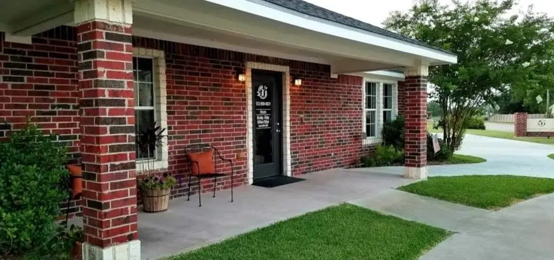 Red brick building with a covered porch and green lawn.