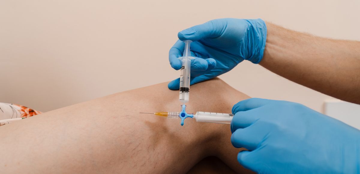 Medical worker gives an injection into a patient’s arm with a syringe and gloved hands.