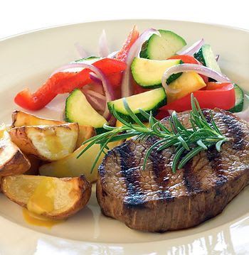 A plate featuring a grilled steak garnished with rosemary, roasted potatoes, and a fresh vegetable medley