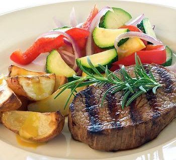 A plate featuring a grilled steak garnished with rosemary, roasted potatoes, and a fresh vegetable medley
