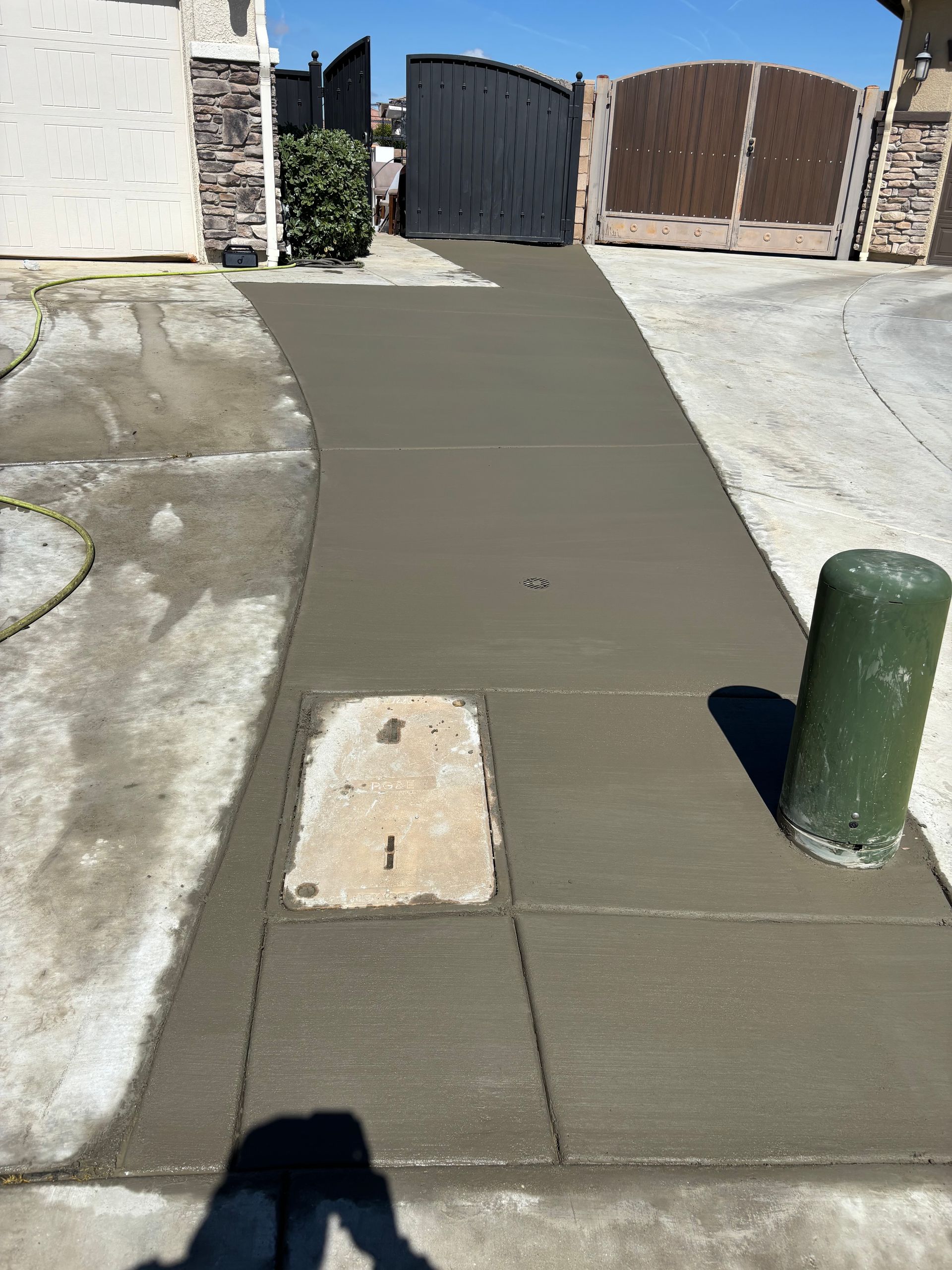 Concrete sidewalk ramp leading to a gated driveway, with a green bollard and curb cut.