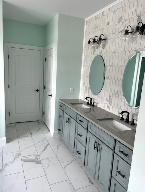 Bright bathroom with mint green walls, double sinks, oval mirrors, and white marble-look tile floor.