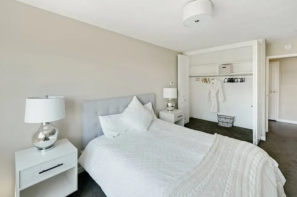 A bedroom with a bed , nightstand , lamp and closet.