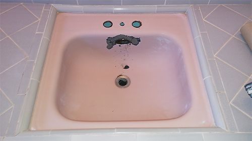 a pink sink in a bathroom with a hole in it .