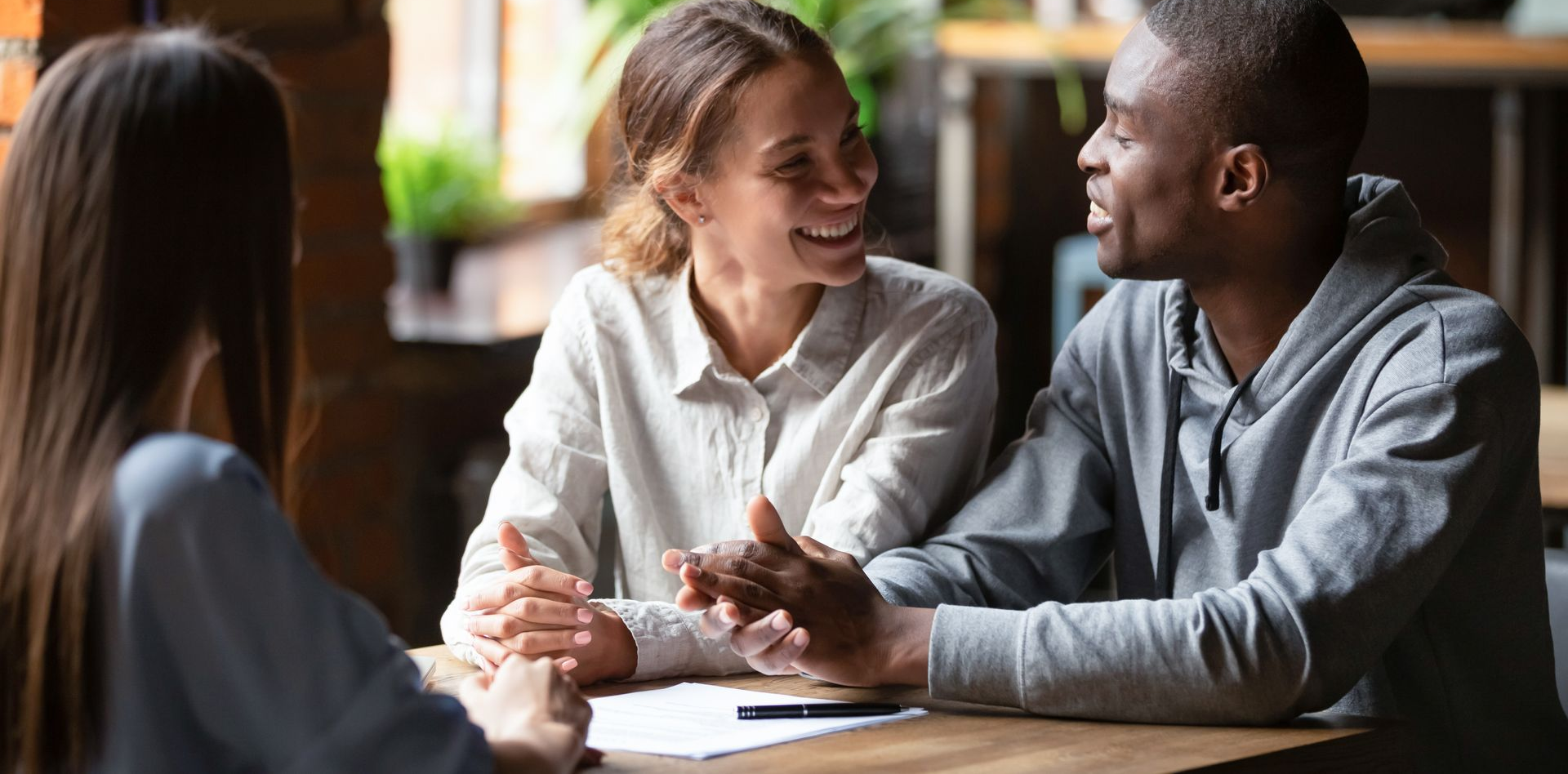 Two coworkers smiling and talking over coffee at a table in a bright office lounge