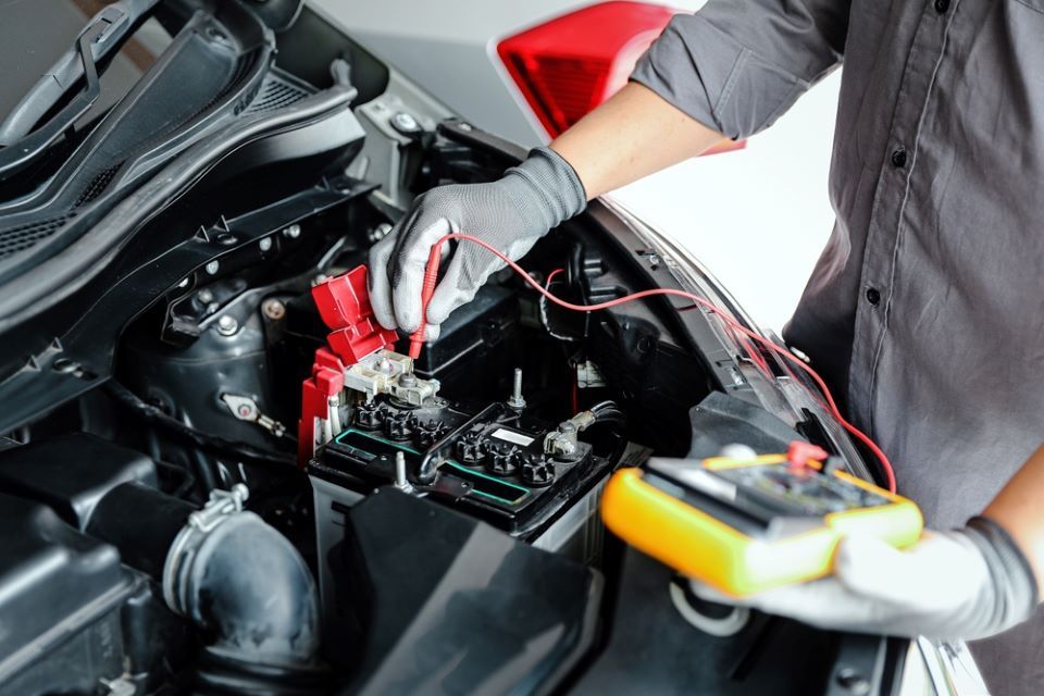 Mechanic testing a car battery with jumper cables in an engine bay