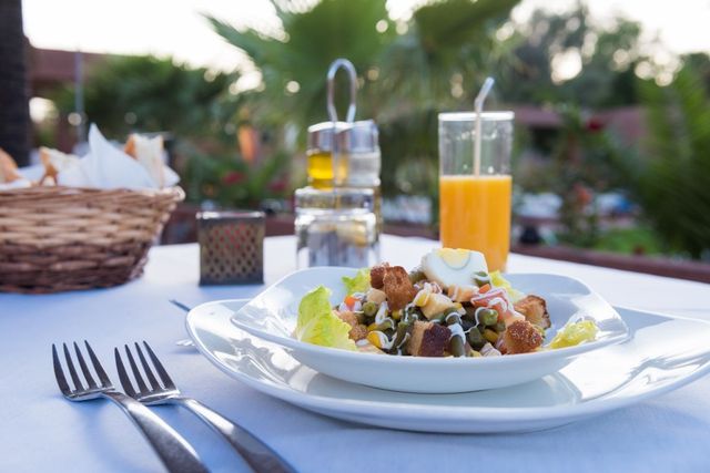 Mesa de jantar ao ar livre com salada, talheres, água e suco de laranja ao pôr do sol.