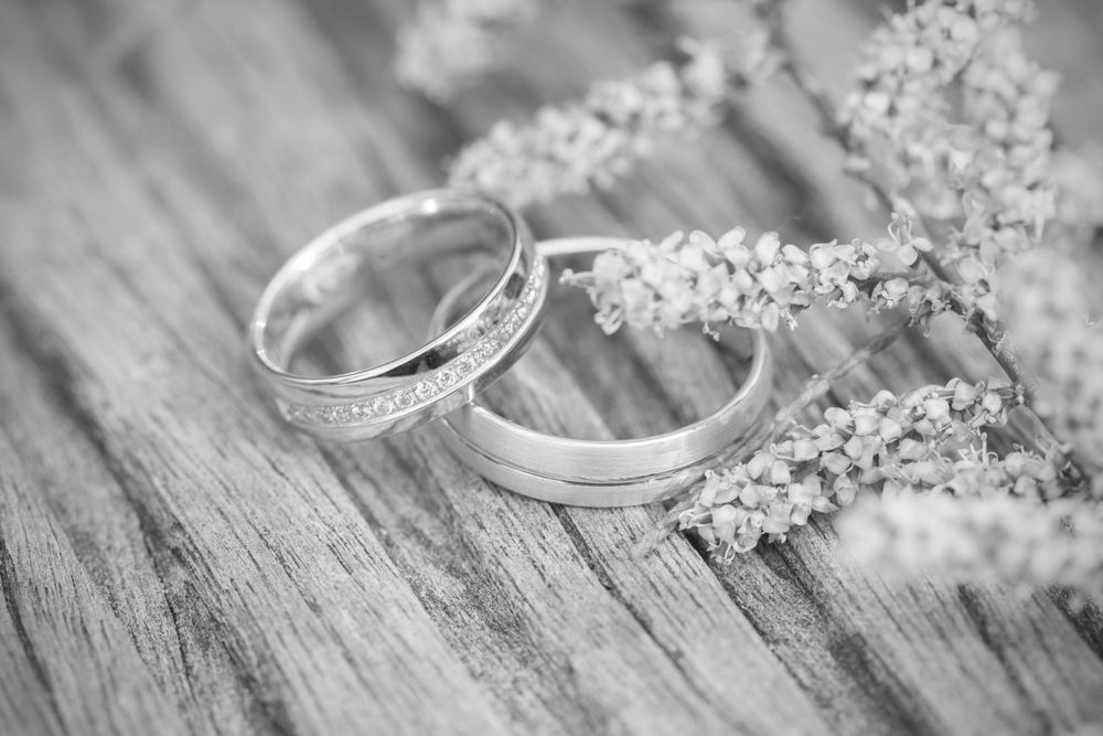 Two silver wedding rings on a rustic wooden surface with delicate flowers nearby - ev law in Bundall, QLD