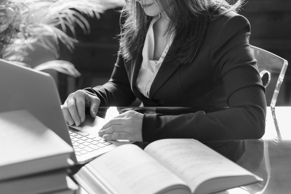 Person working at a desk with a laptop and open book in black and white. - ev law in Bundall, QLD