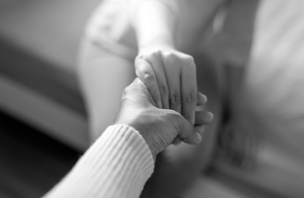 Close-up of two hands gently holding each other on a couch - ev law in Bundall, QLD