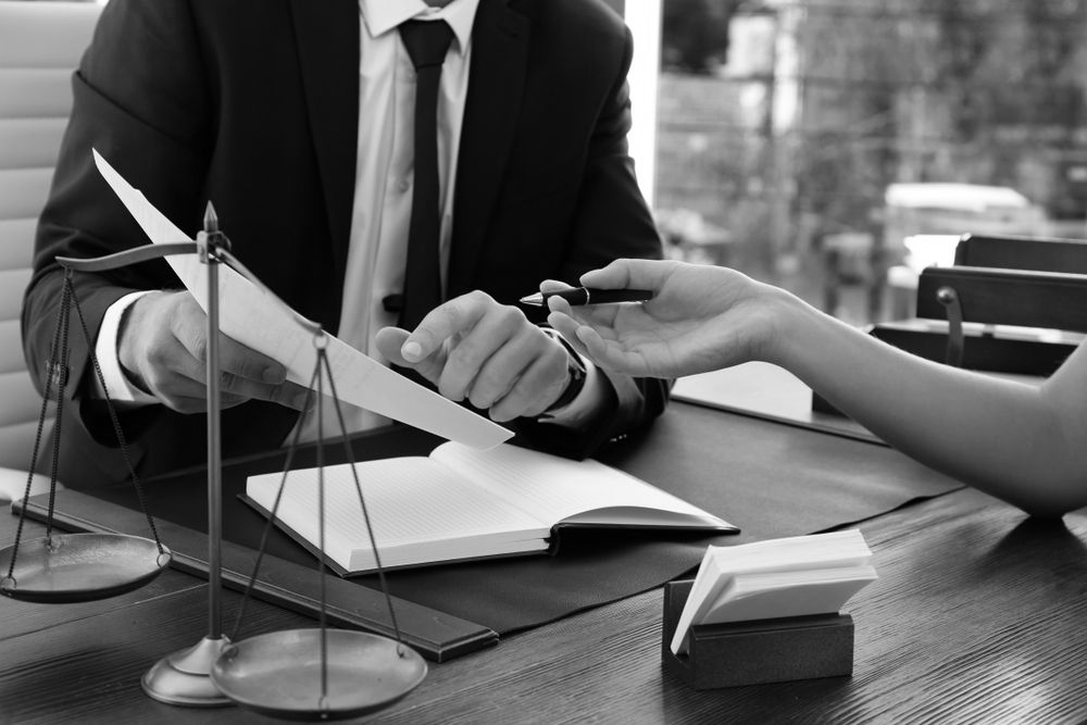 Business meeting with legal contract signing, scales of justice and pen on a desk - ev law in Bundall, QLD