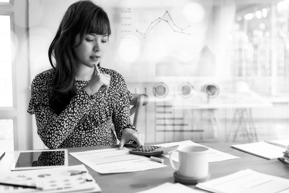 Woman working at a desk with papers, laptop, coffee cup, and charts on a bright office table - ev law in Bundall, QLD