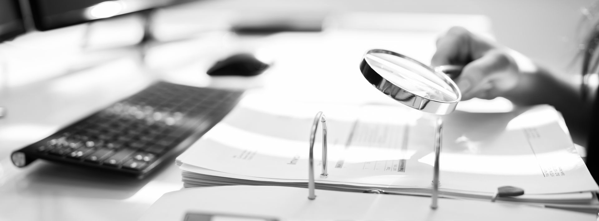 Desk with calculator, pen, open binder, and magnifying glass over paperwork in black and white. - ev law in Bundall, QLD