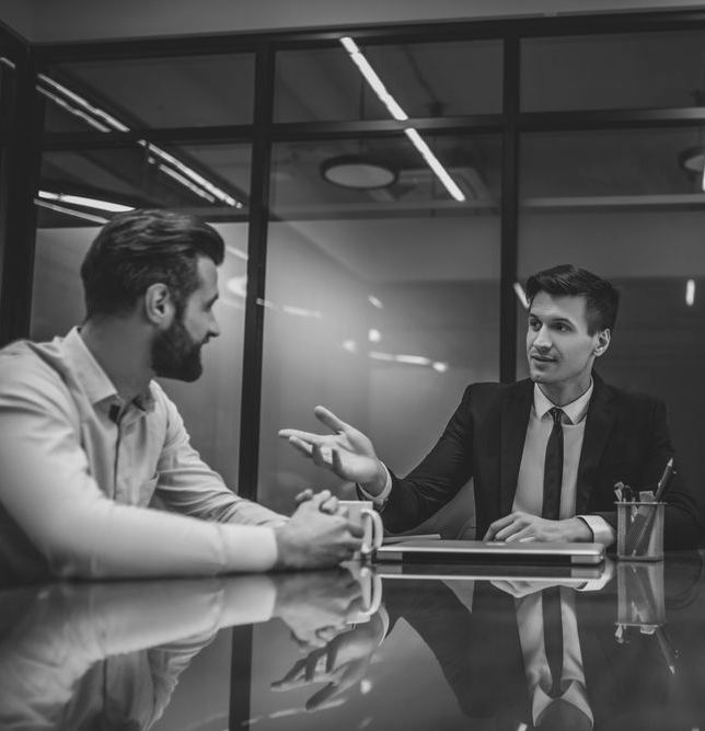 Two people in business attire talking across a conference table in a modern office - ev law in Bundall, QLD