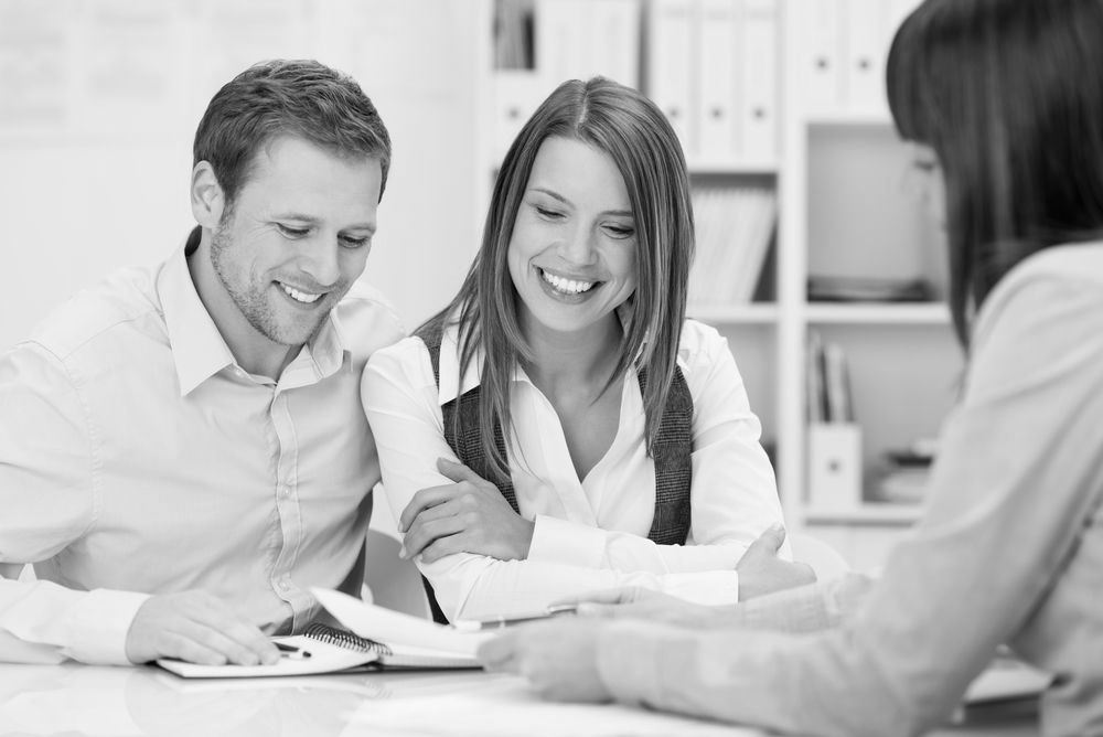 Two smiling people reviewing documents with a consultant at a table in an office - ev law in Bundall, QLD