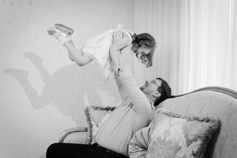 Person lifts a smiling child on a sofa in a bright living room. - ev law in Bundall, QLD
