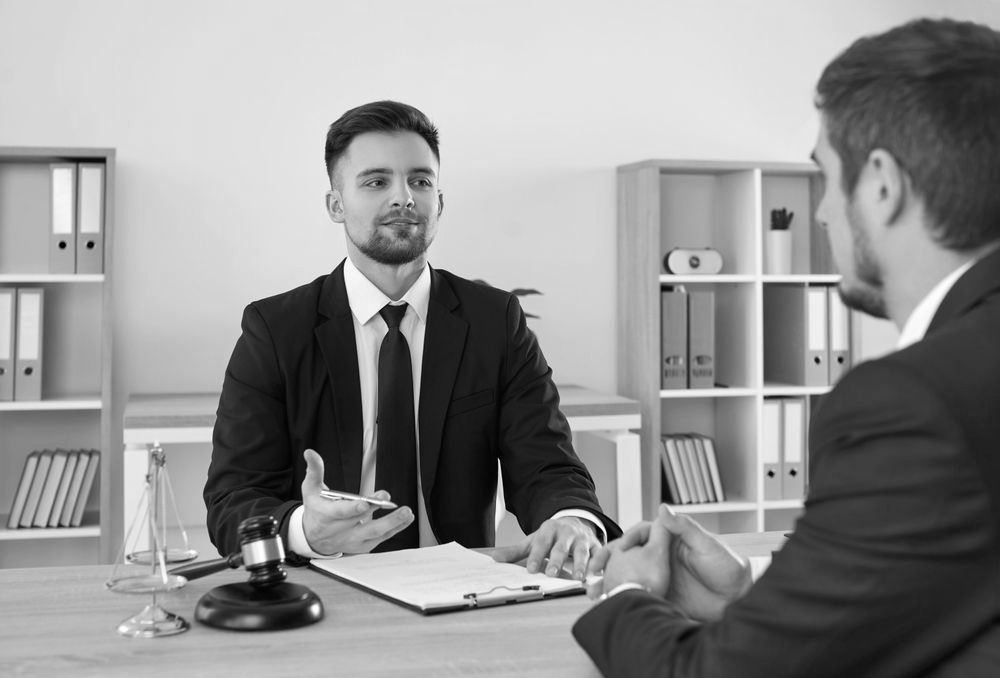 Two men in suits discussing a document across an office desk, with shelves and a gavel nearby. - ev law in Bundall, QLD