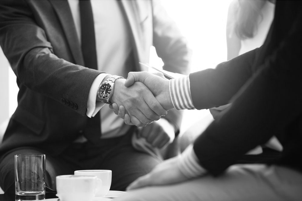 Two people in suits shaking hands across a table in a bright office setting - ev law in Bundall, QLD