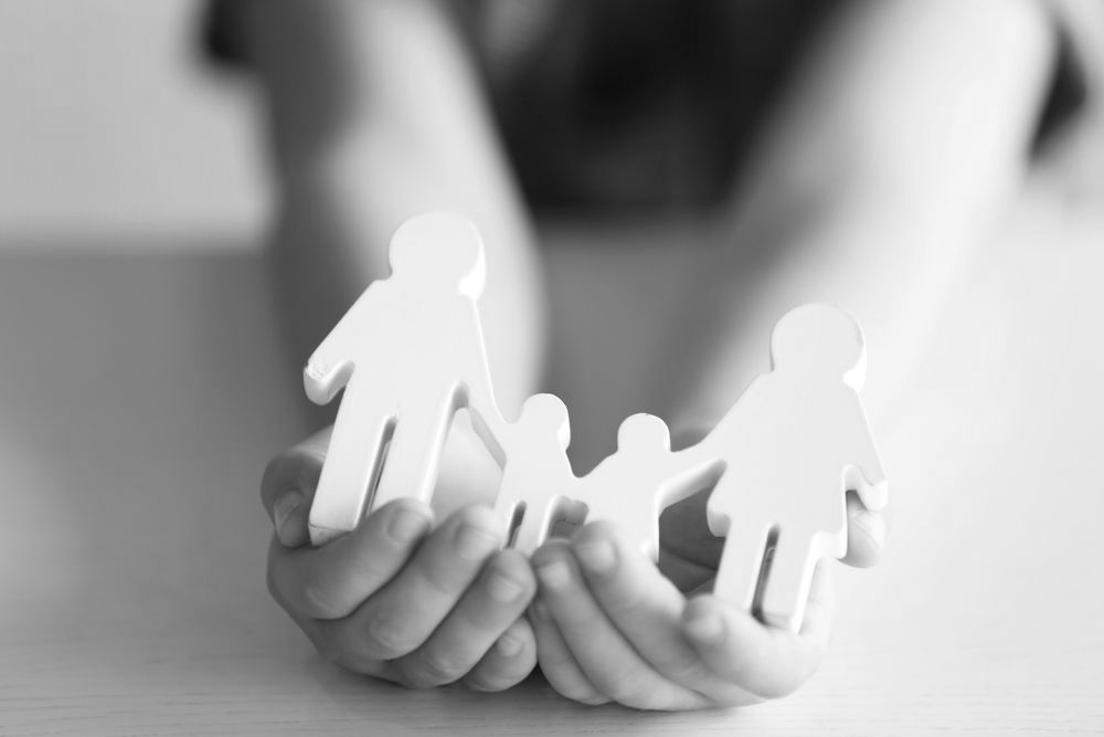 Hands holding white paper cutouts of a family on a blurred gray background - ev law in Bundall, QLD