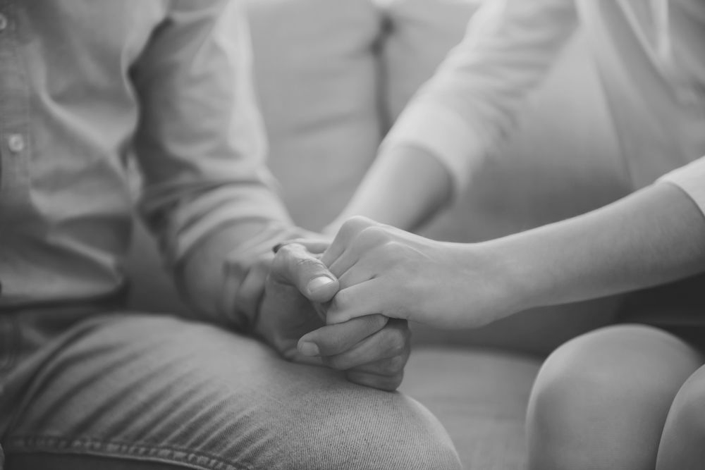 Two people holding hands in a grayscale close-up, seated on a couch - ev law in Bundall, QLD