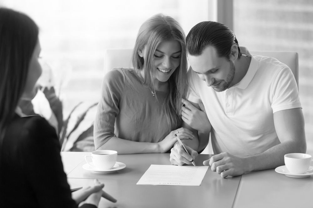 Two people reviewing a document at a table while a seated woman listens nearby, with coffee cups on the table. - ev law in Bundall, QLD
