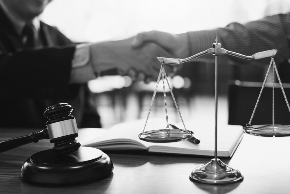 Gavel, scales, and open law book on a desk with blurred handshake in the background - ev law in Bundall, QLD