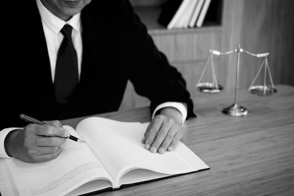 Lawyer in black suit writing in open notebook beside scales of justice on a desk - ev law in Bundall, QLD