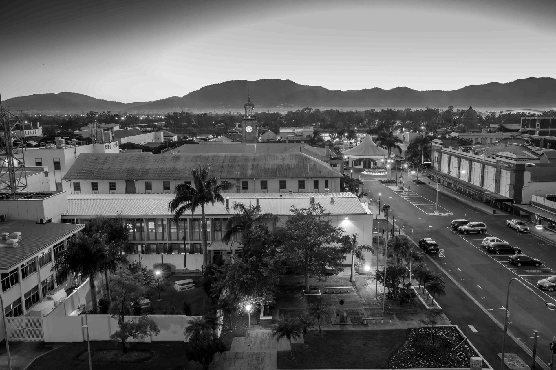 Twilight view of a city street with lit buildings, palm trees, and mountains in the background - ev law in Bundall, QLD