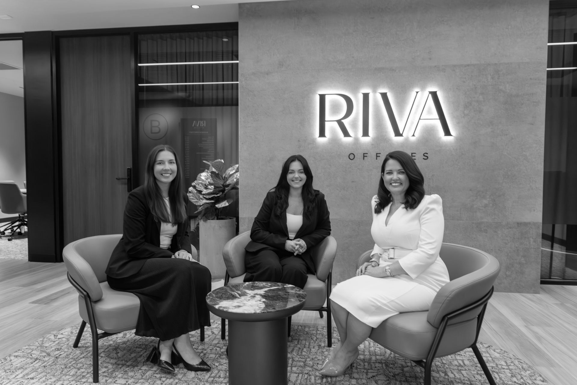 Three people seated in a modern office lobby beneath a glowing RIVA sign. - ev law in Bundall, QLD